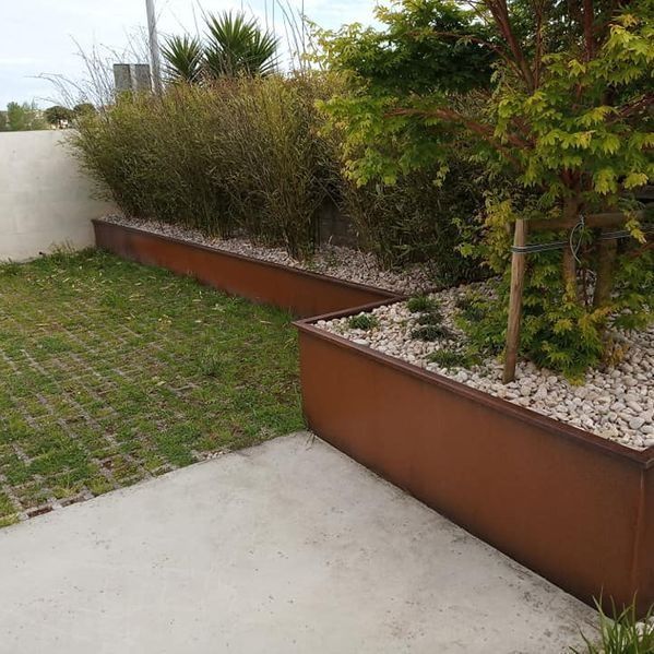 Una hilera de jardineras marrones llenas de plantas y grava en un jardín.