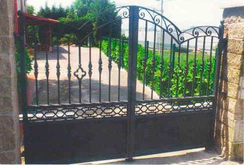 Una puerta de hierro forjado negro se abre a un camino de entrada.