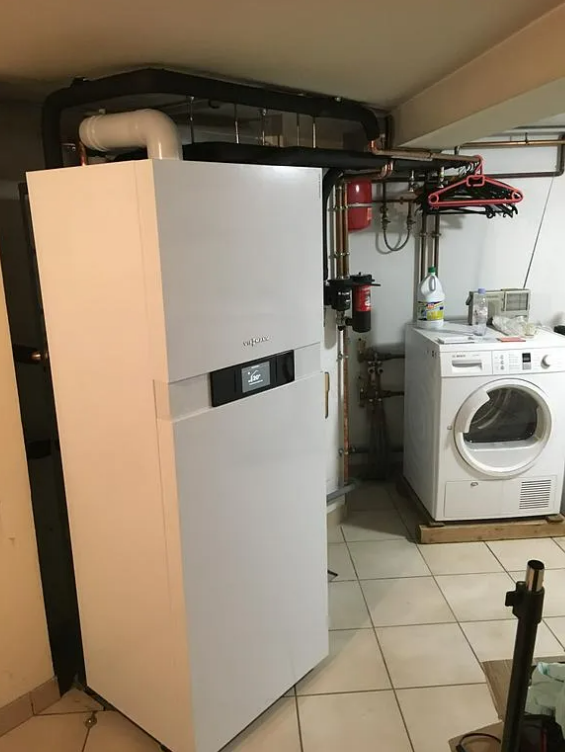 Un gros appareil de chauffage blanc et un sèche-linge se trouvent dans le sous-sol. 
