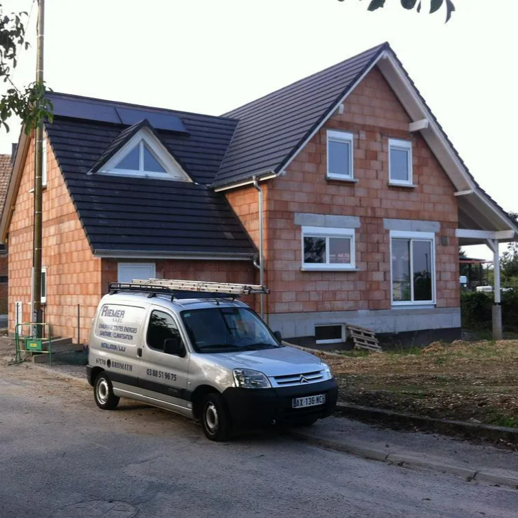 Le véhicule de Sarl Riemer est garé devant une maison en construction, avec une façade en briques.