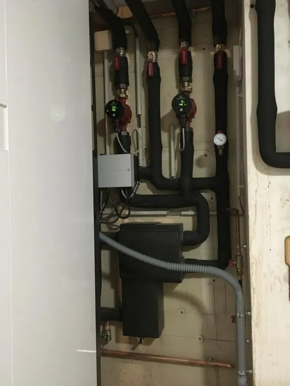 Réseau de plomberie avec tuyaux isolés noirs, pompes et manomètres fixés au mur.