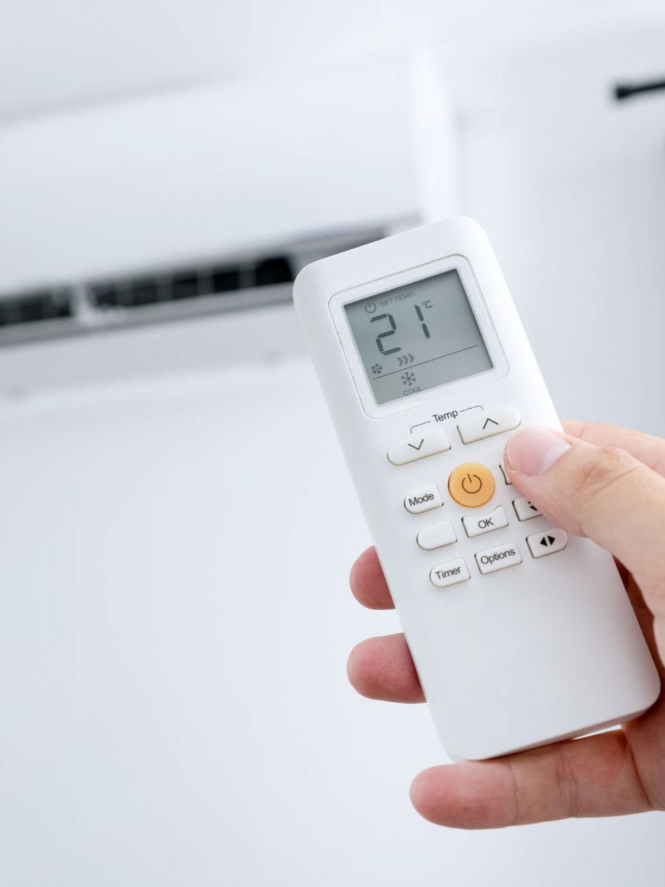 Main tenant une télécommande blanche de climatiseur, pointant vers un climatiseur mural.