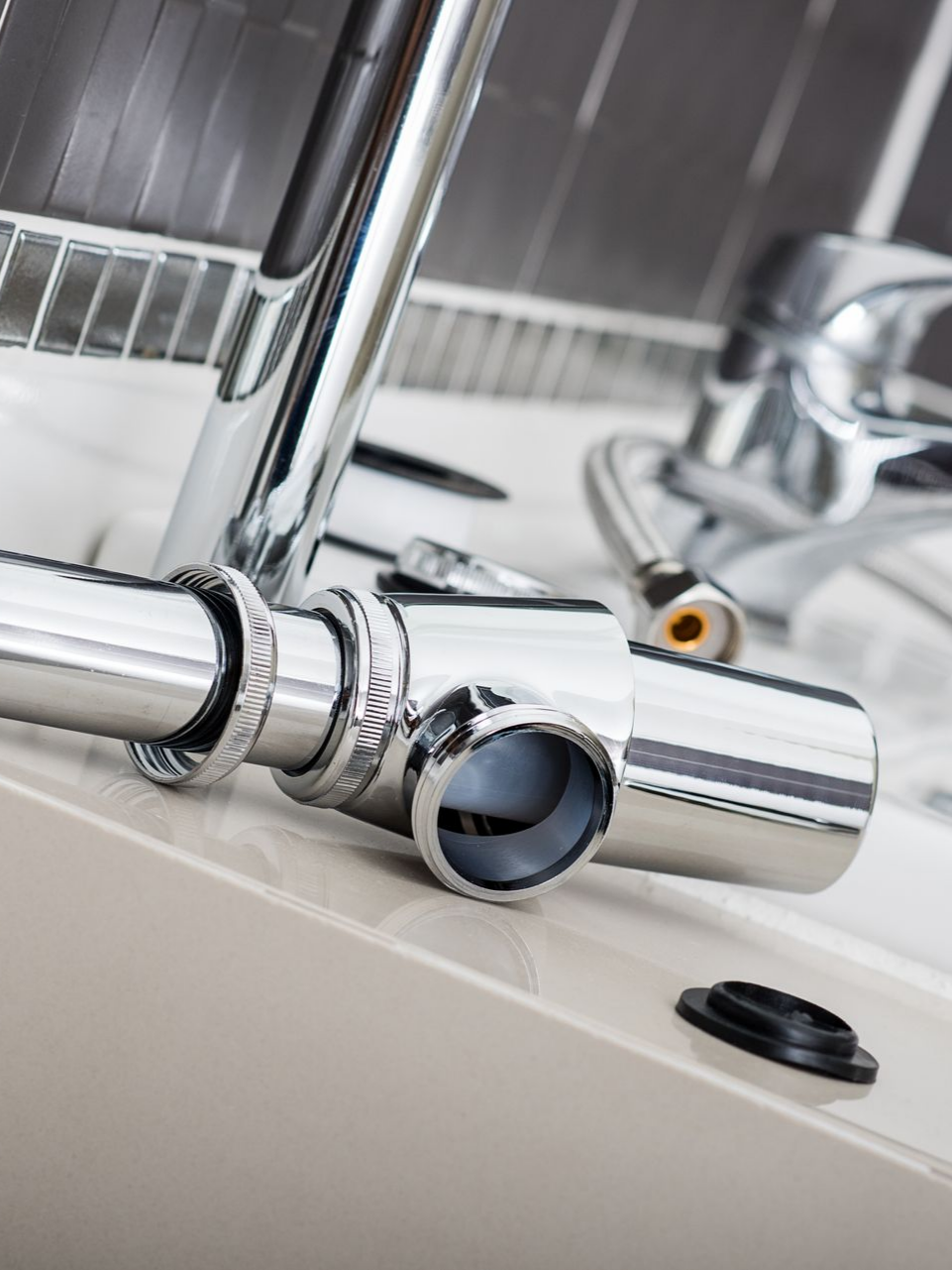 Accessoires de plomberie chromés sur une surface blanche ; des tuyaux, un robinet et des flexibles.