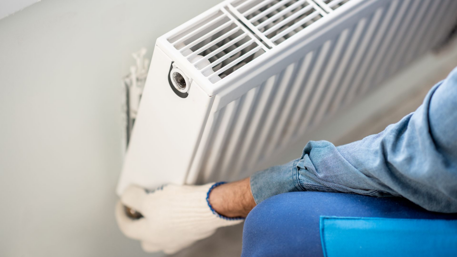 Une personne portant des gants fixe un radiateur blanc au mur.