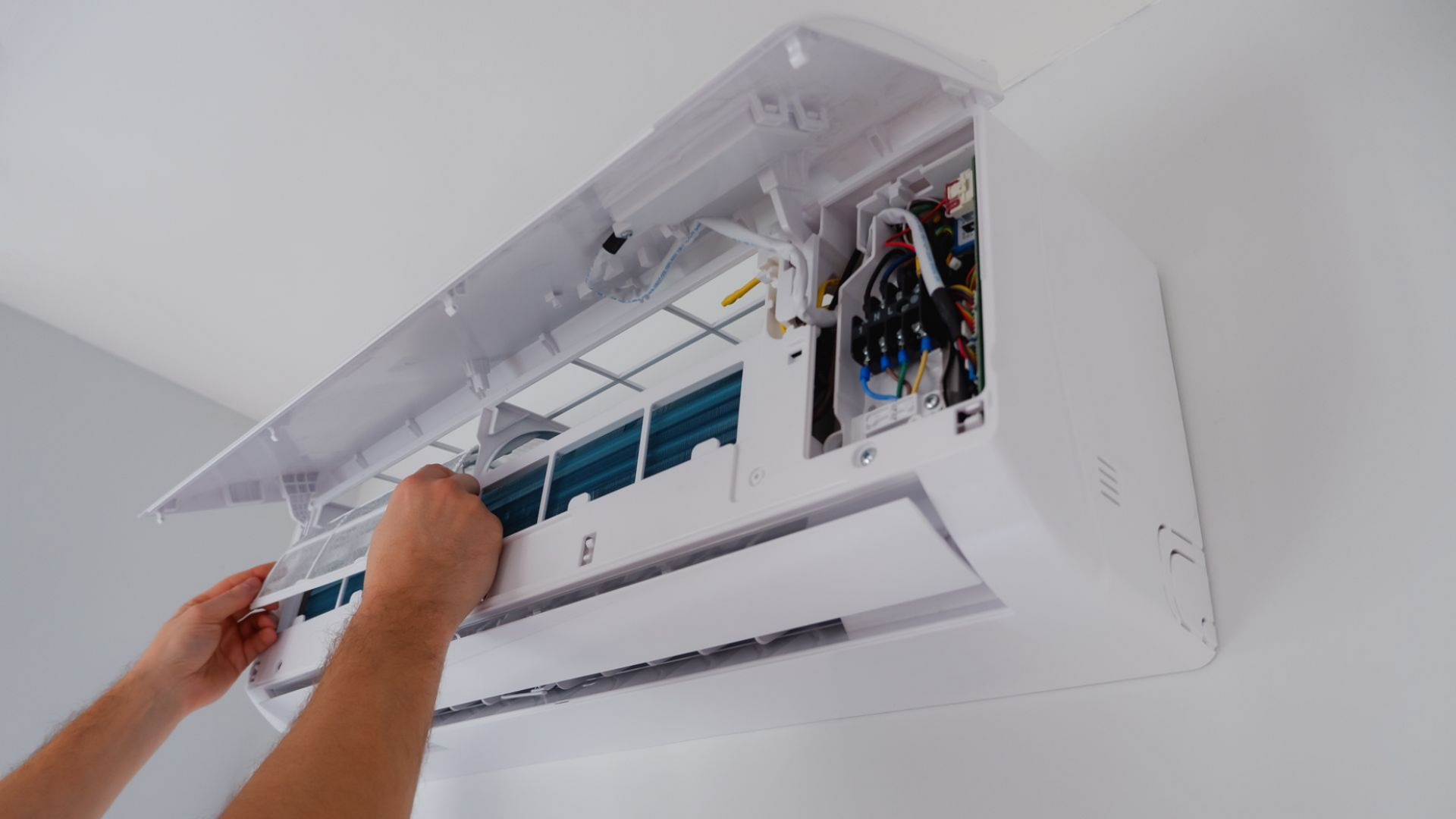 Une personne retire le filtre à air d'un climatiseur mural blanc.
