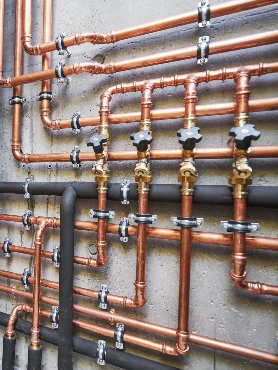 Tuyaux de cuivre avec vannes et isolation noire contre un mur en béton.