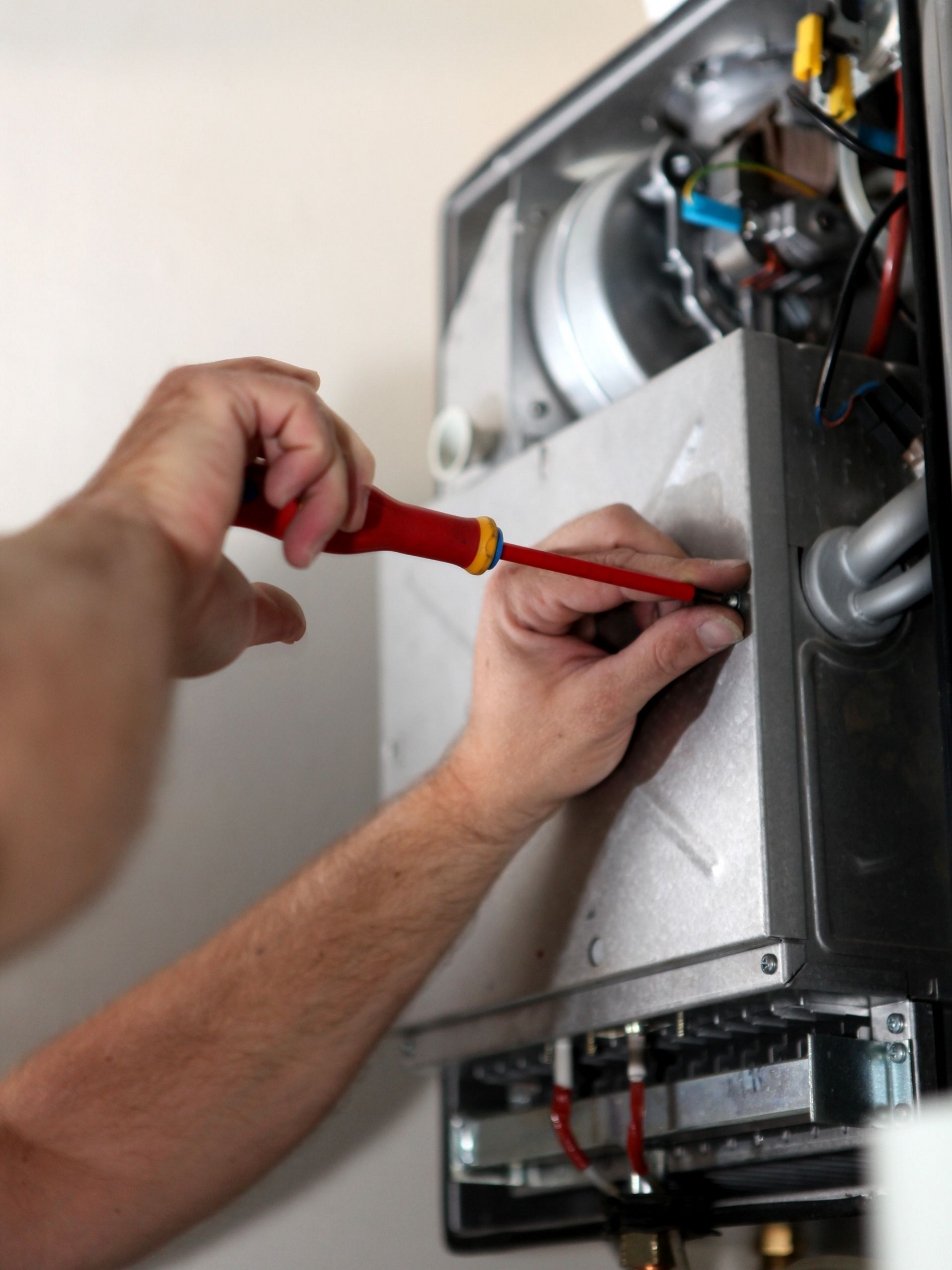 Une personne utilise un tournevis pour travailler sur une chaudière à gaz.