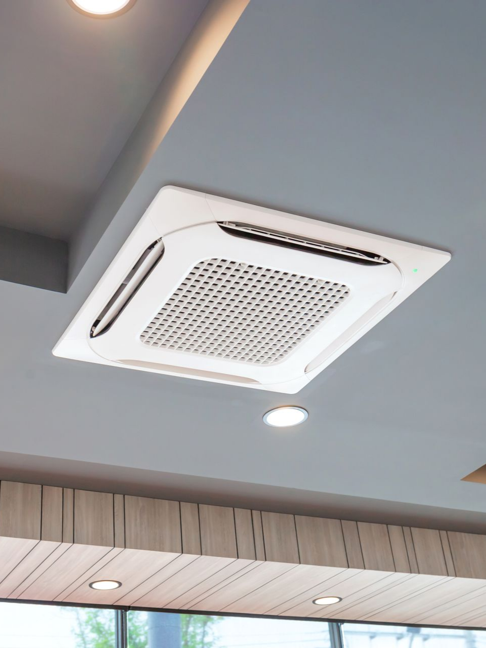 Climatiseur blanc fixé au plafond, sur un plafond gris.