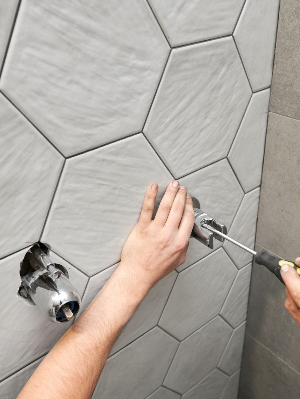 Personne installant un robinet de douche chromé sur un mur carrelé.