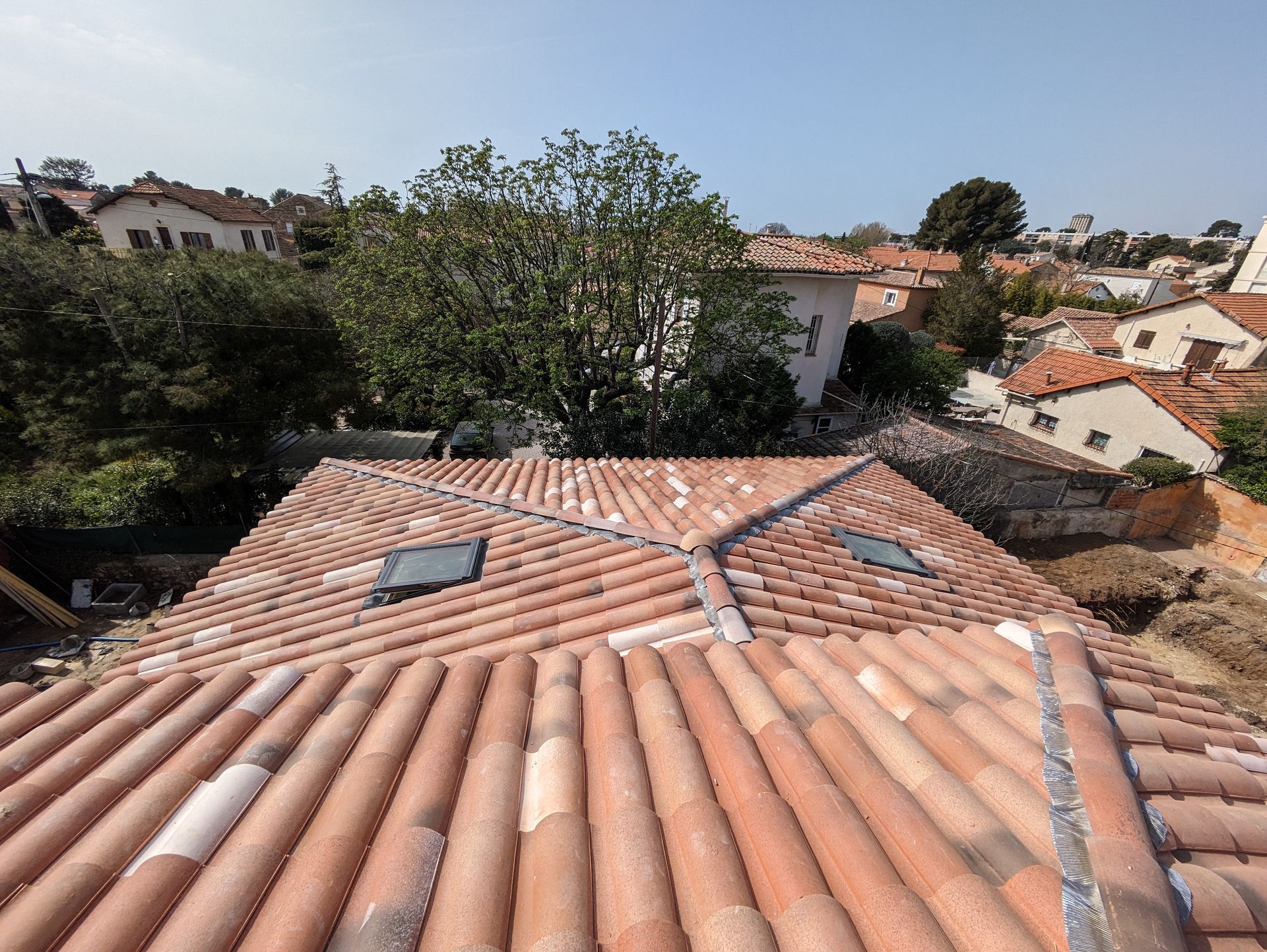 Un homme installe des tuiles rouges sur un toit.