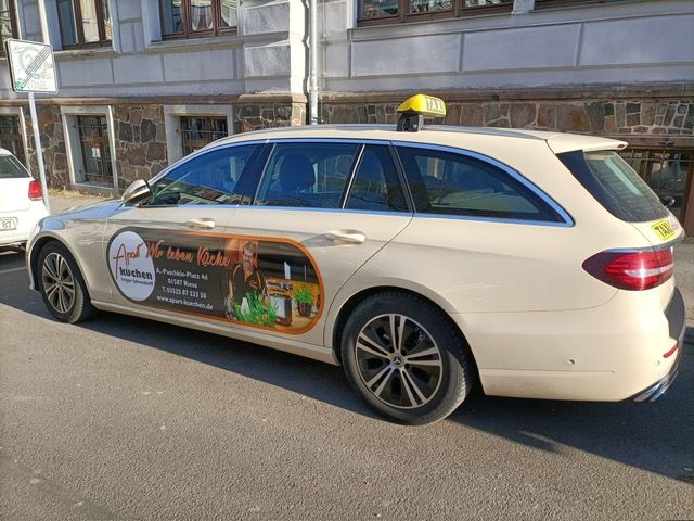 Ein Mann lächelt im Auto und nimmt die Schlüssel von einem Verkäufer entgegen. Eine Frau lächelt auf dem Beifahrersitz. Innenansicht eines Autohauses.