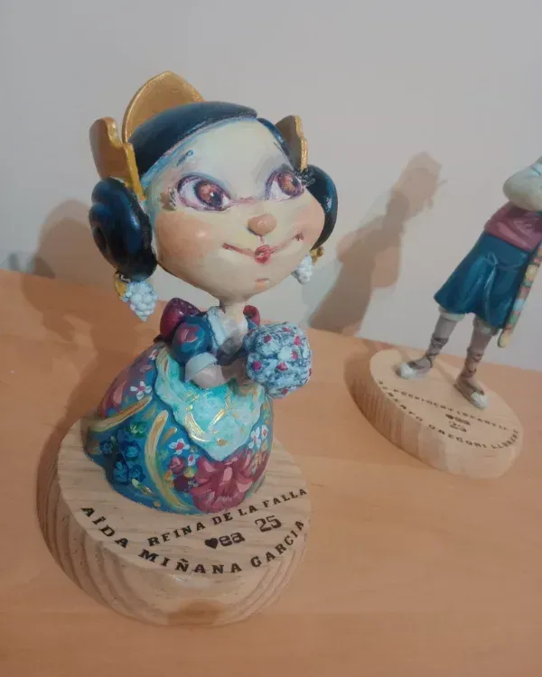 Dos figuritas decorativas sobre una superficie de madera; un personaje de pelo azul se encuentra en primer plano.