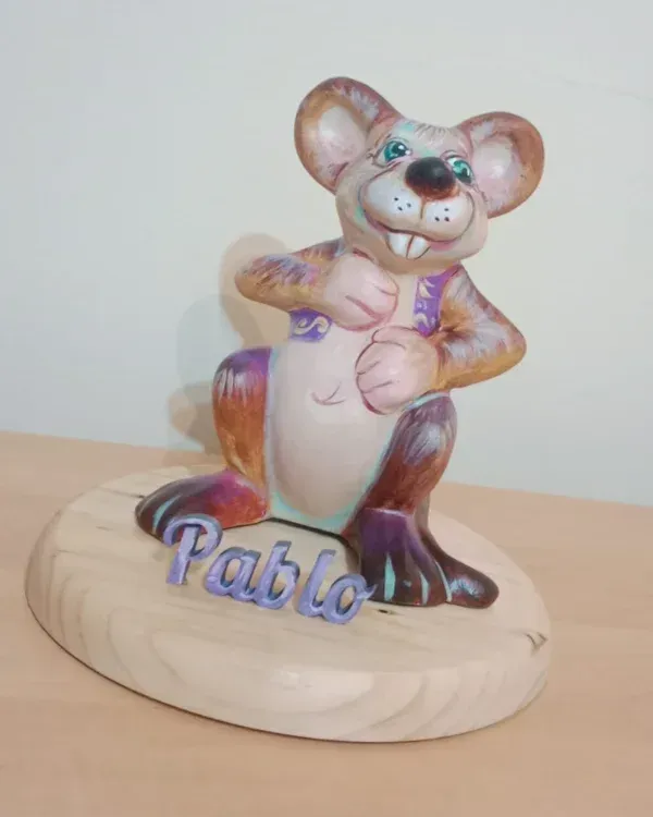 Figurita de ratón de madera sobre una base redonda con el nombre “Pablo” pintado en azul.