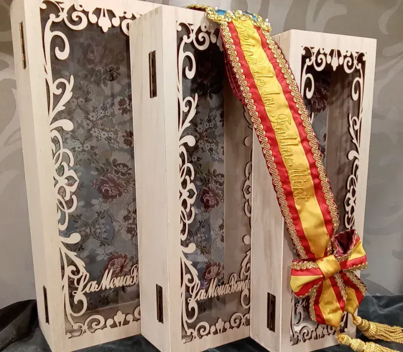 Armario decorativo de madera blanca con elaborados recortes y una cinta roja y amarilla que lo cubre.