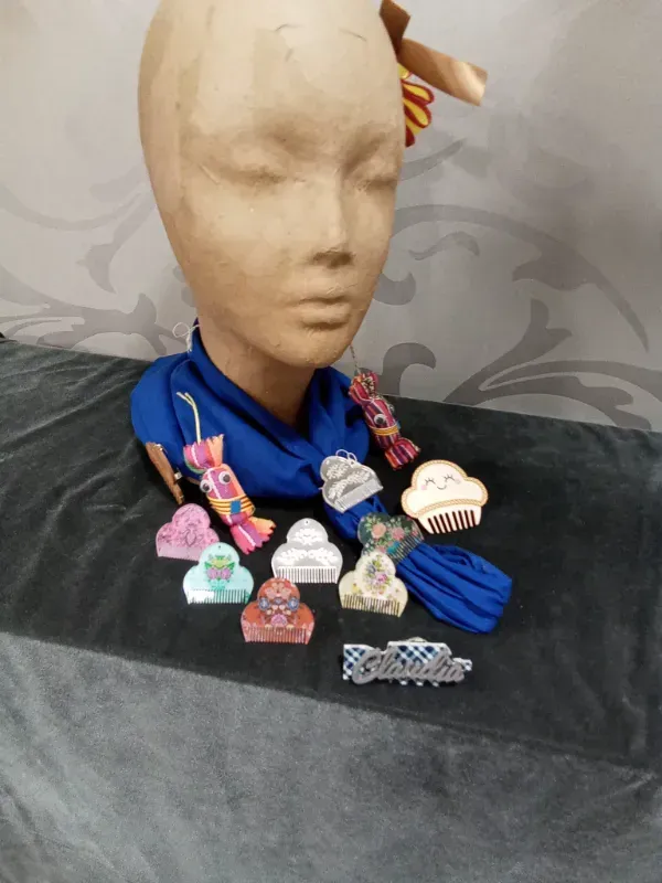 Cabeza de maniquí con bufanda azul y broches de colores, expuesta sobre un fondo de tela negra.