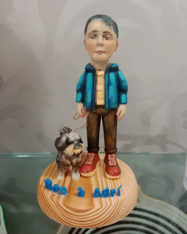Pequeña figurita hecha a mano de una persona con un perro sobre una base redonda de madera con letras azules.