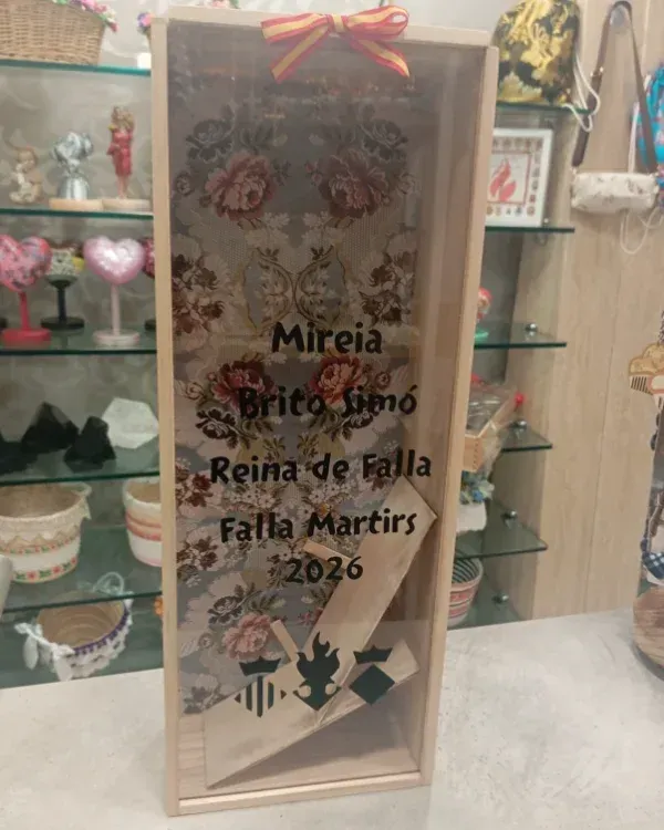 Placa decorativa con diseño floral y texto en honor a “Mireia” como Reina de Falla 2026 en una vitrina.