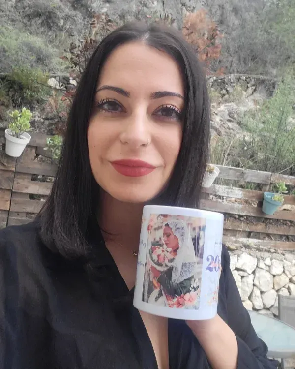 Mujer al aire libre sosteniendo una taza blanca con un colorido diseño floral, sonriendo a la cámara.