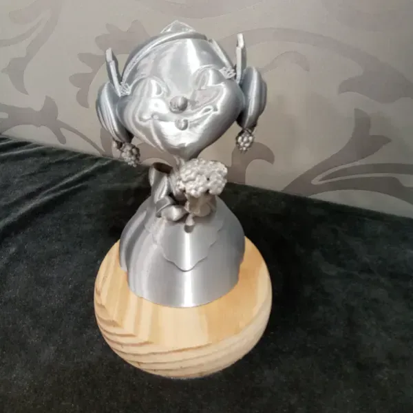 Busto de figura plateada con auriculares sobre una base de madera sobre un fondo de tela oscura.