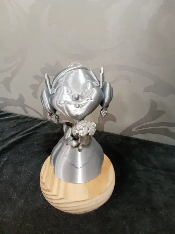 Figurita plateada con auriculares sobre una base de madera, sosteniendo pequeñas flores blancas.