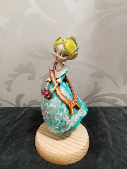 Pequeña figurita decorativa de una niña con un vestido turquesa sobre una base de madera.