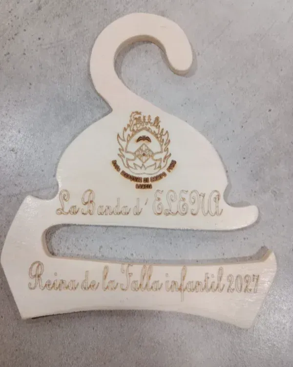 Placa blanca de madera con forma de percha, con escudo y texto en español sobre una superficie gris.