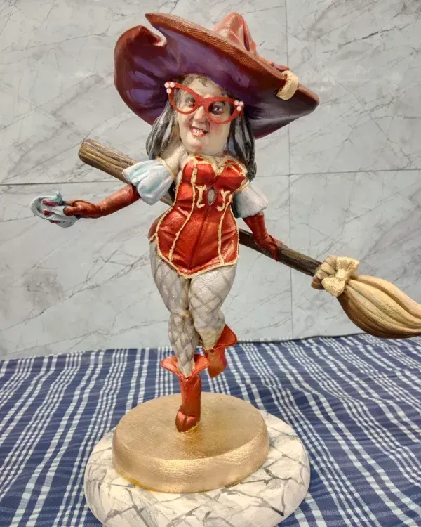 Figura de bruja caprichosa con vestido rojo y sombrero morado, de pie sobre una escoba sobre una base.