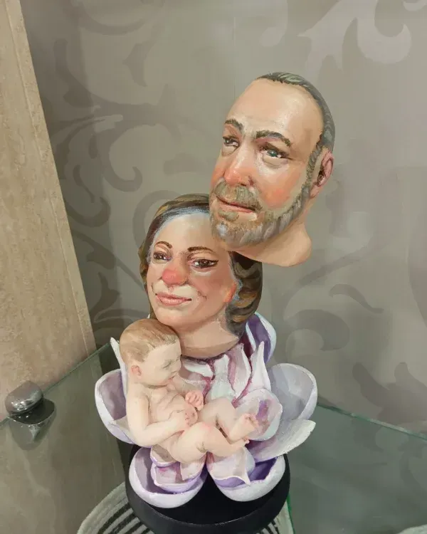 Una pequeña figurita pintada que representa a dos adultos sosteniendo a un bebé, sobre una repisa de cristal.