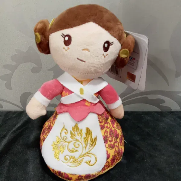 Muñeca de peluche pequeña con cabello castaño, vestido rosa y blanco y motivos decorativos dorados