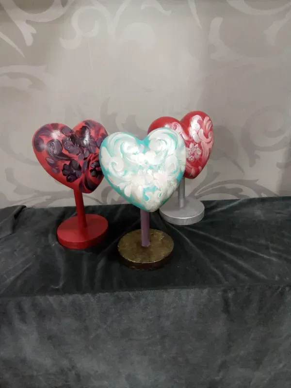 Tres globos decorativos en forma de corazón, sujetos con palitos, de color rojo, blanco y menta.