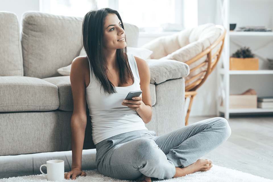 Eine Frau sitzt mit einem Mobiltelefon in der Hand vor einem Sofa auf dem Boden.