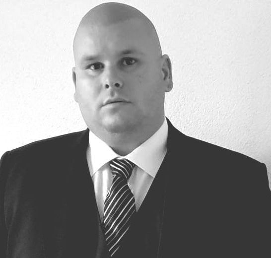 Ein kahlköpfiger Mann in Anzug und Krawatte schaut in die Kamera