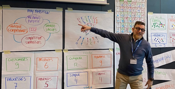 Un hombre está parado frente a una pizarra y la señala.