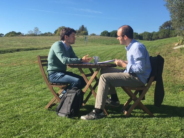Dos hombres están sentados en una mesa en el césped hablando entre ellos.