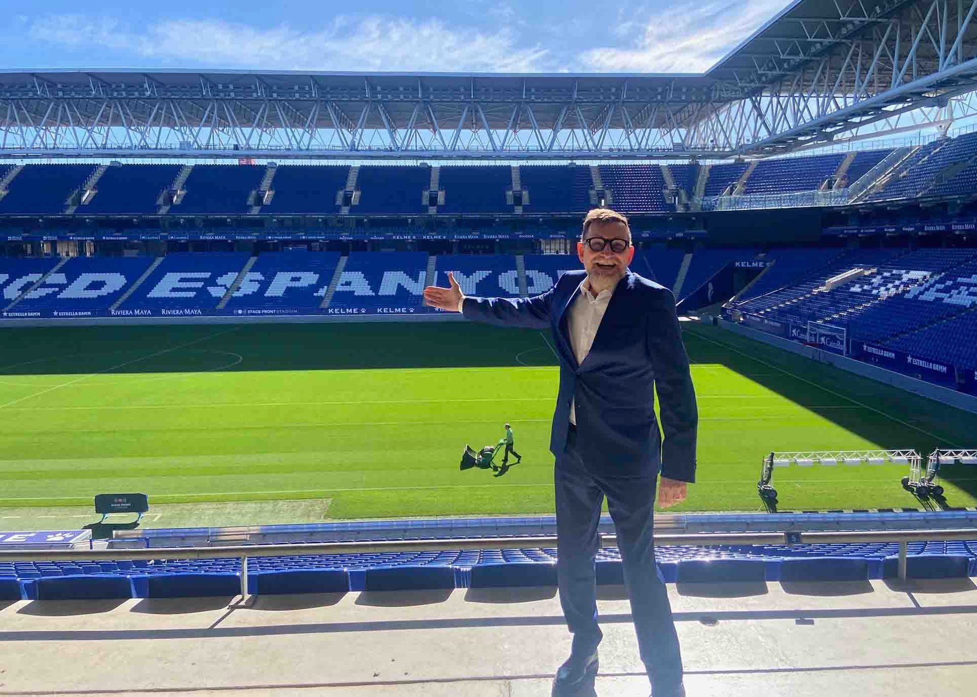 Un hombre con traje está parado frente a un estadio de fútbol.