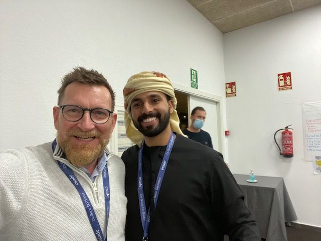 Dos hombres posando para una foto en una habitación con un extintor de incendios al fondo.
