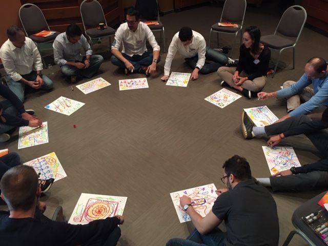 Un grupo de personas está sentado en círculo con dibujos en el suelo.