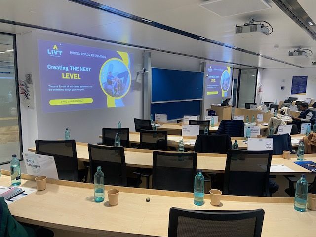 Una sala grande con mesas y sillas y una pantalla de proyector en la pared.