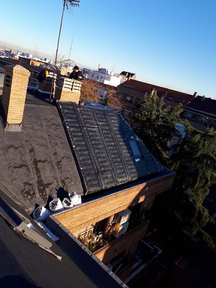 Azotea con paneles solares, una chimenea y edificios de la ciudad a lo lejos bajo un cielo azul despejado.