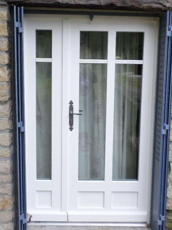 Portes françaises blanches avec panneaux de verre et volets décoratifs.