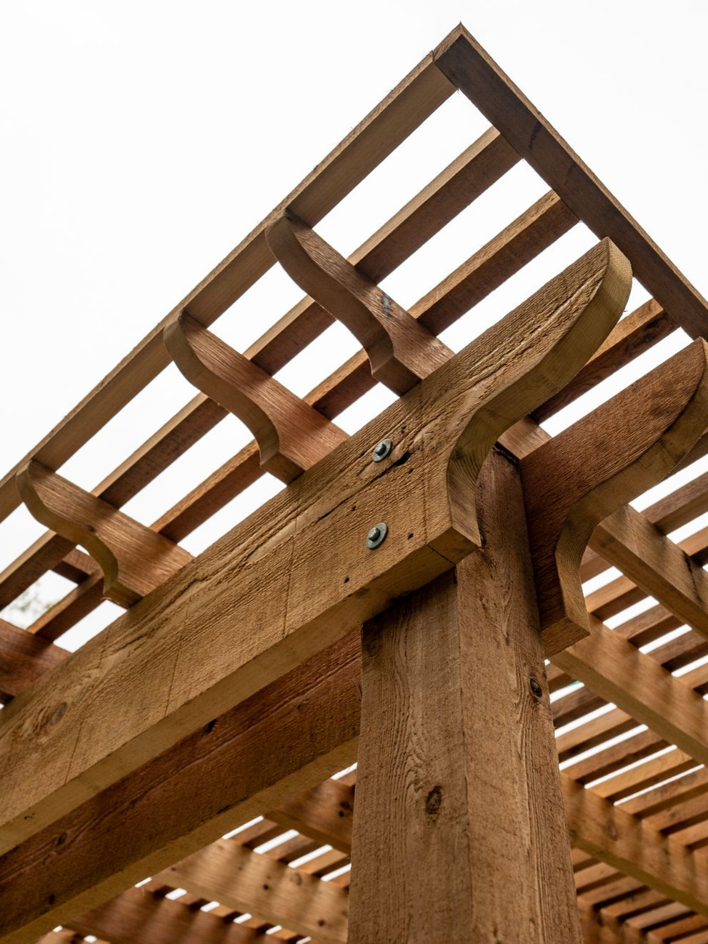 Pergola d'angle en bois, avec supports décoratifs, sur fond de ciel lumineux.