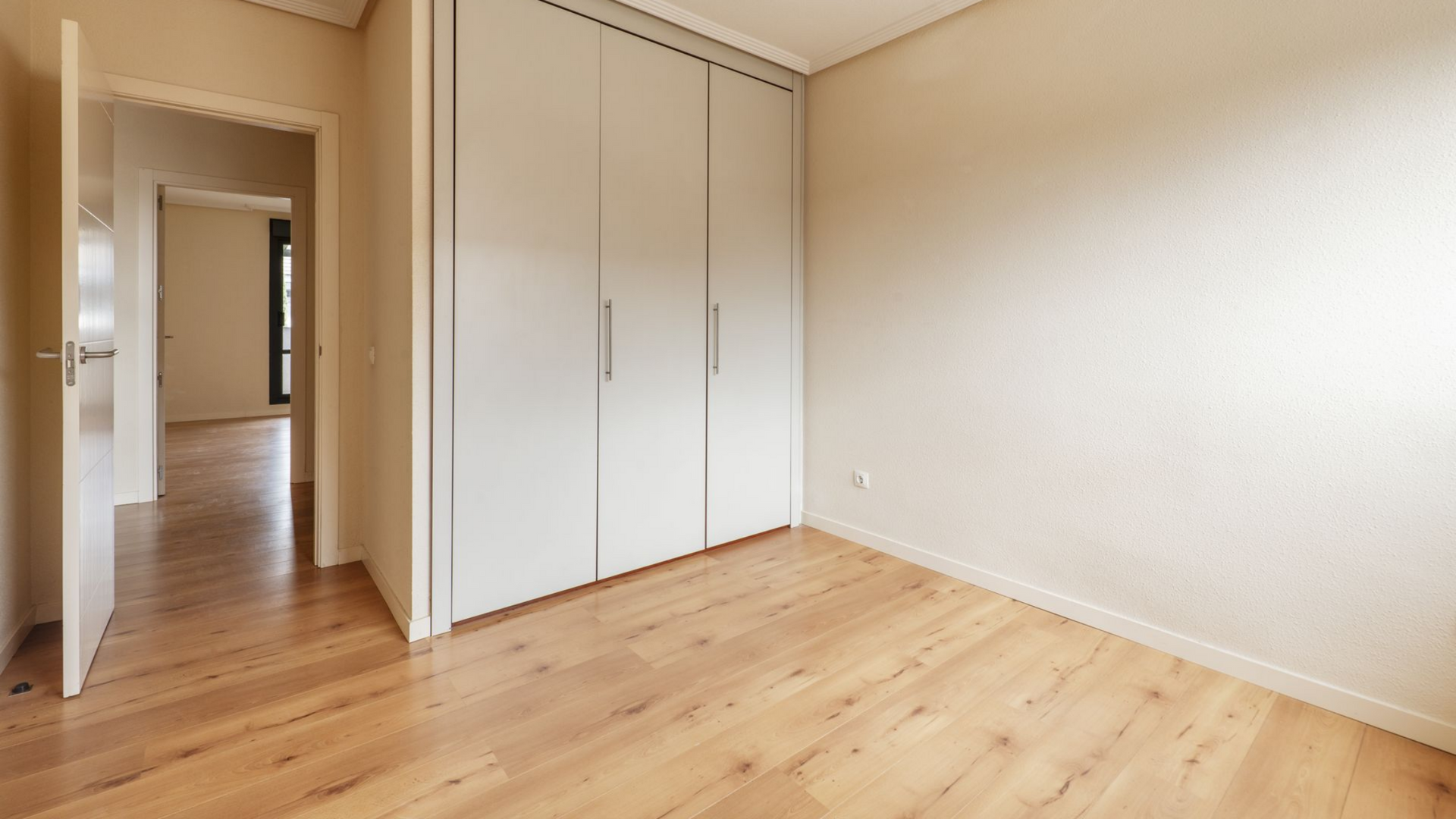 Chambre vide avec parquet, placard blanc et porte donnant sur le couloir.