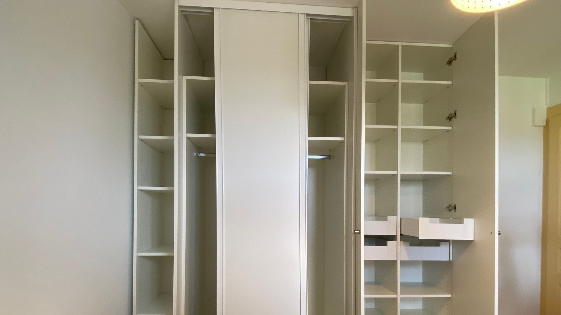 Armoire encastrée blanche avec étagères, penderie et tiroirs, ouverte dans une pièce.