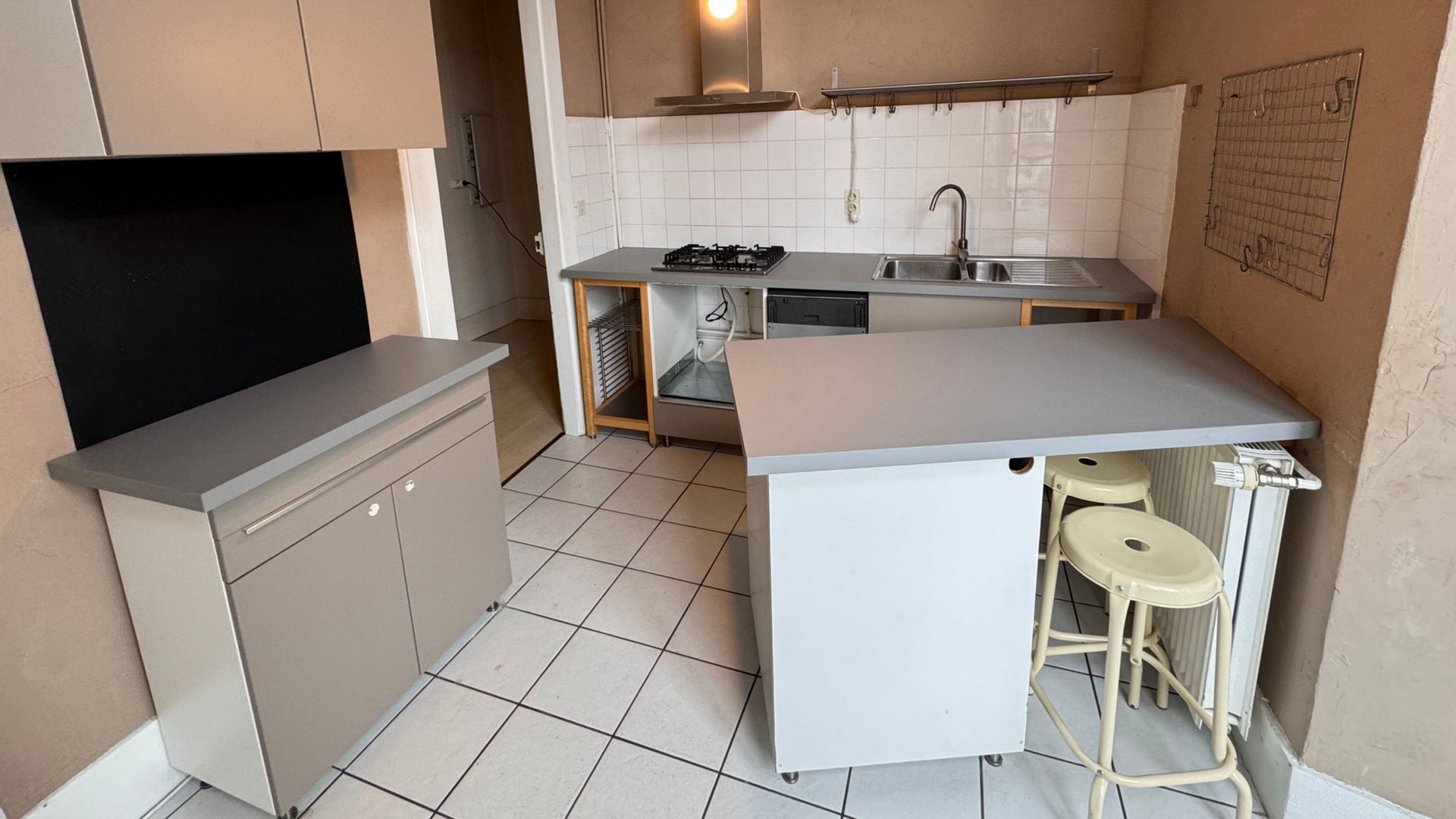 Petite cuisine avec placards, comptoirs et évier. Deux tabourets de bar sont installés à côté du comptoir.