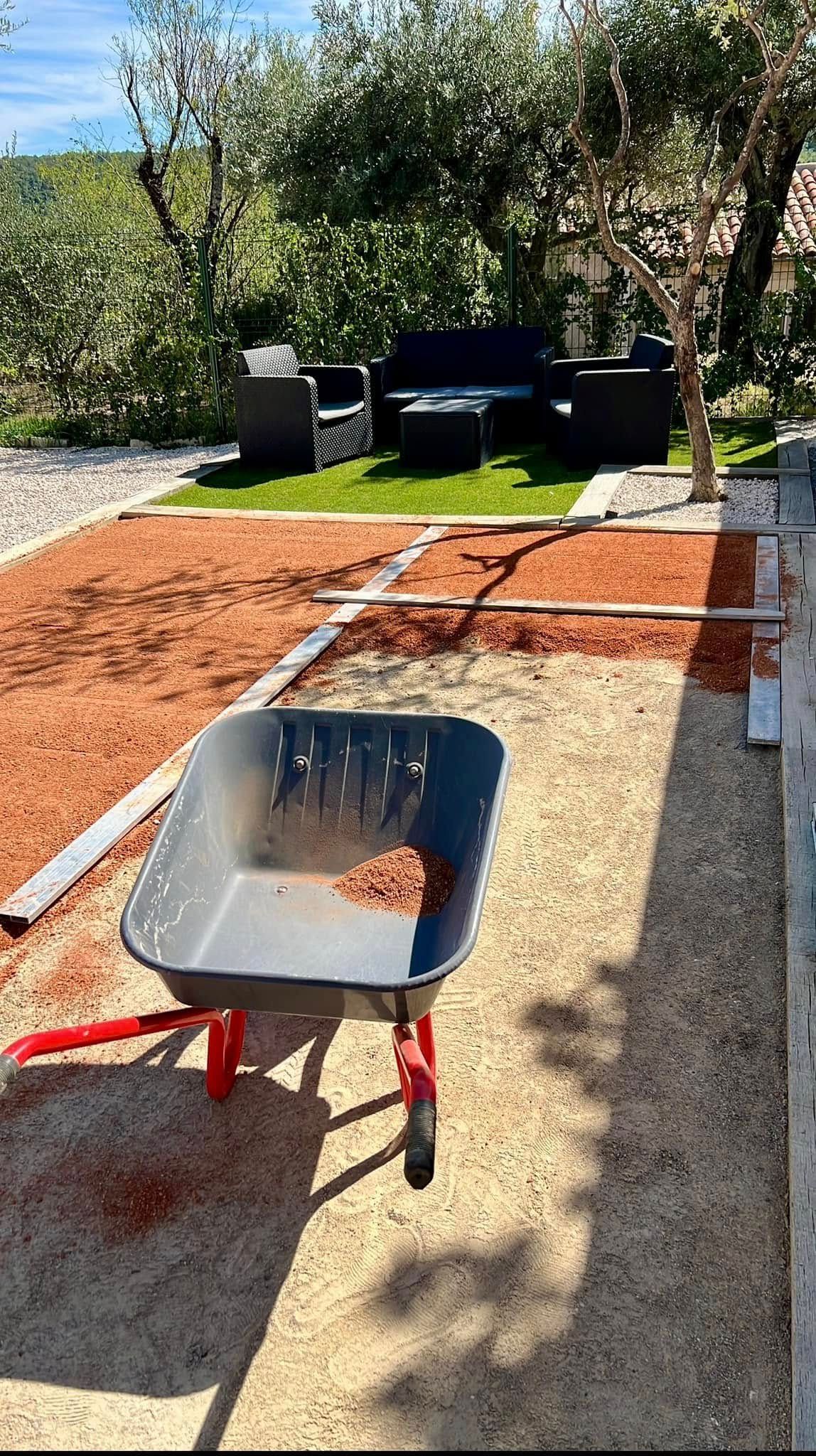 Une brouette en train de couvrir un terrain de pétanque de terre battue