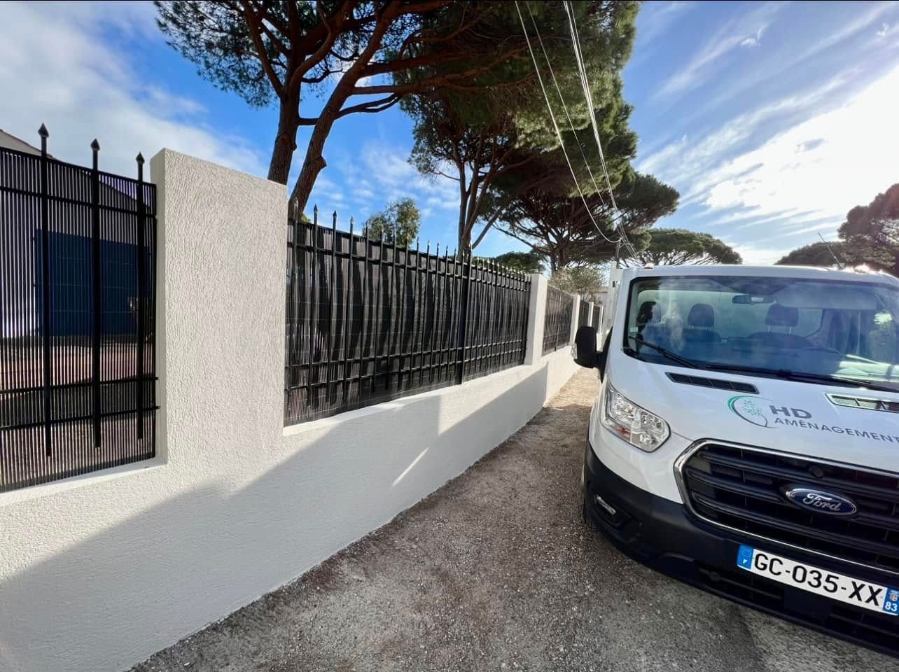 Mur en crépi et clôture de fer avec un camion