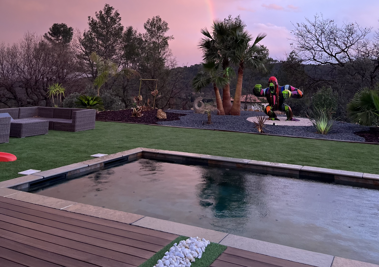 Une piscine entre une terrasse en bois et du gazon avec un gorille