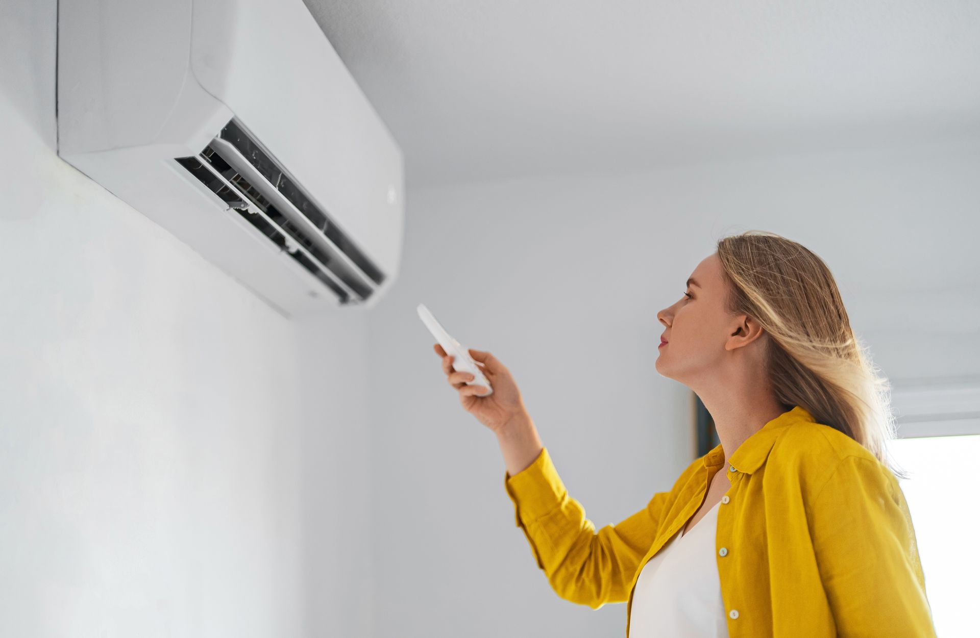 Une femme utilise une télécommande pour faire fonctionner un climatiseur fixé sur un mur.