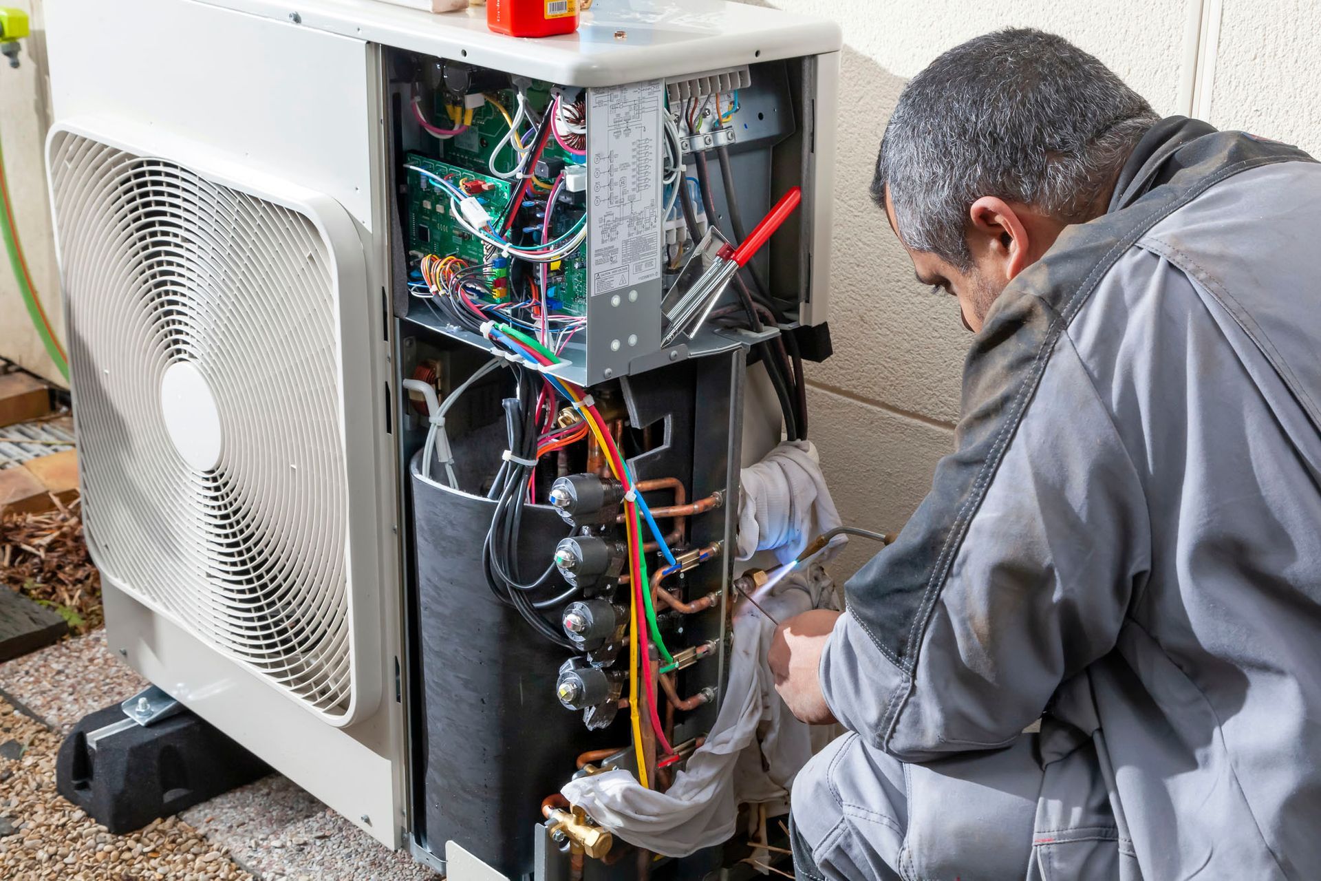 Un homme en tenue de travail répare une pompe à chaleur.