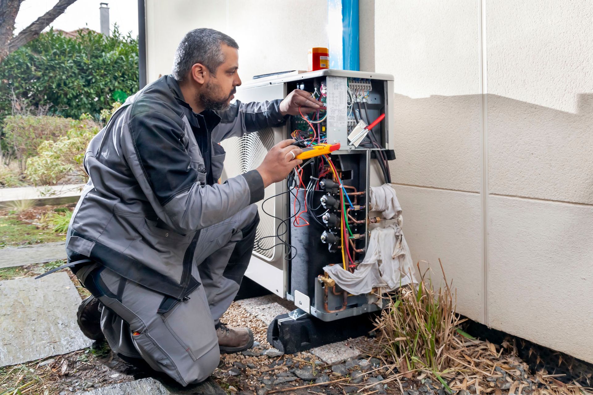 Un homme en tenue de travail est agenouillé et utilise un multimètre pour inspecter un appareil.